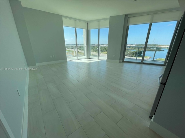 unfurnished room featuring a water view, light wood-type flooring, and floor to ceiling windows