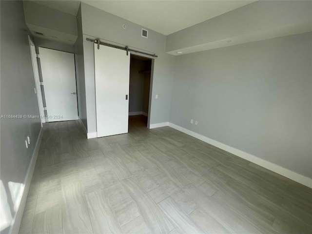 unfurnished bedroom featuring light wood-type flooring, a barn door, a walk in closet, and a closet