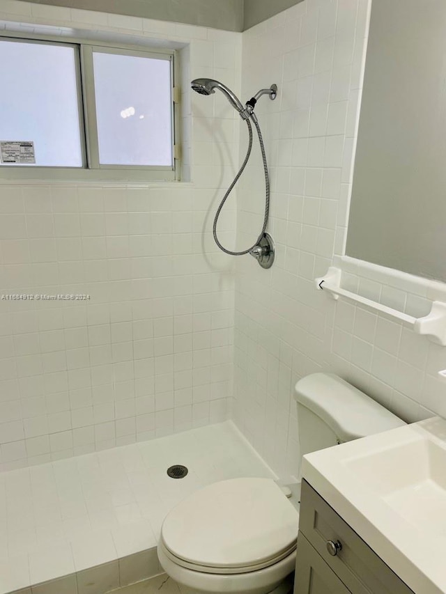 bathroom with vanity, toilet, tile walls, and tiled shower