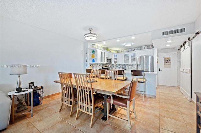 dining room featuring a textured ceiling, a barn door, and light tile patterned floors