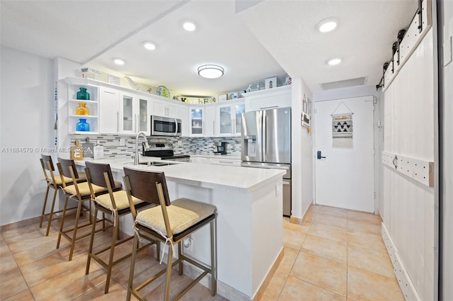 kitchen featuring a kitchen breakfast bar, kitchen peninsula, a barn door, white cabinets, and appliances with stainless steel finishes