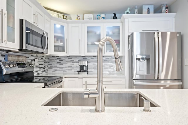 kitchen featuring appliances with stainless steel finishes, white cabinets, light stone counters, and backsplash