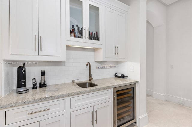 kitchen featuring decorative backsplash, white cabinets, beverage cooler, light stone countertops, and sink