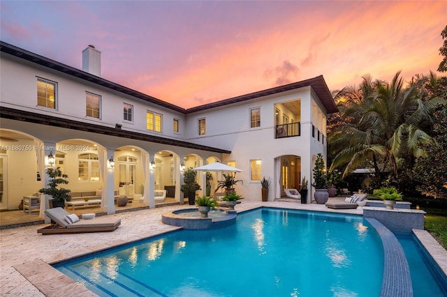 back house at dusk featuring a patio area, a pool with hot tub, and a balcony