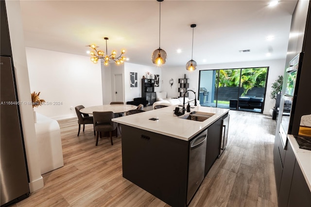 kitchen with sink, decorative light fixtures, light hardwood / wood-style flooring, an inviting chandelier, and a kitchen island with sink