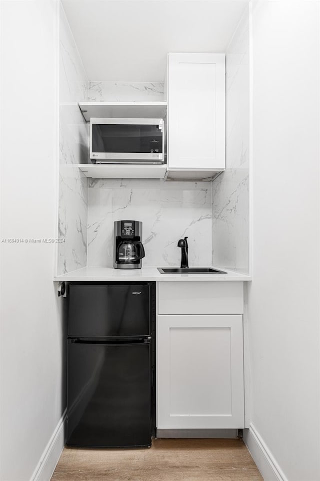 bar featuring black fridge, white cabinets, decorative backsplash, sink, and light hardwood / wood-style flooring