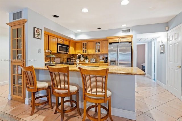 kitchen with stainless steel appliances, light tile patterned floors, light stone counters, and backsplash