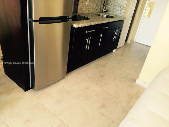 kitchen with black electric stovetop, tasteful backsplash, sink, light stone counters, and stainless steel refrigerator