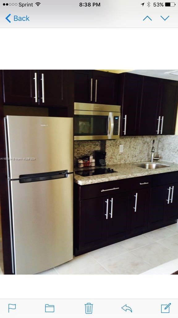 kitchen with dark brown cabinets, sink, light tile patterned floors, appliances with stainless steel finishes, and tasteful backsplash