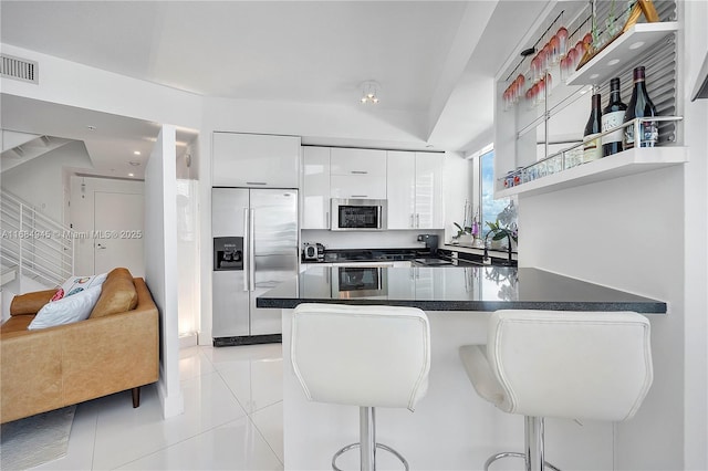 kitchen with stainless steel appliances, a breakfast bar, white cabinets, open shelves, and dark countertops