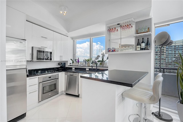 kitchen with stainless steel appliances, dark countertops, white cabinetry, and a kitchen breakfast bar