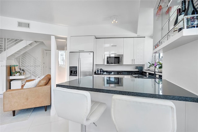 kitchen featuring visible vents, white cabinets, dark countertops, a peninsula, and stainless steel appliances