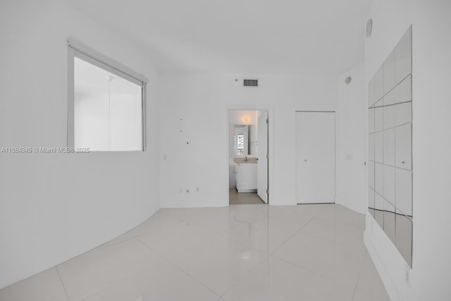 unfurnished bedroom with visible vents, connected bathroom, and light tile patterned floors