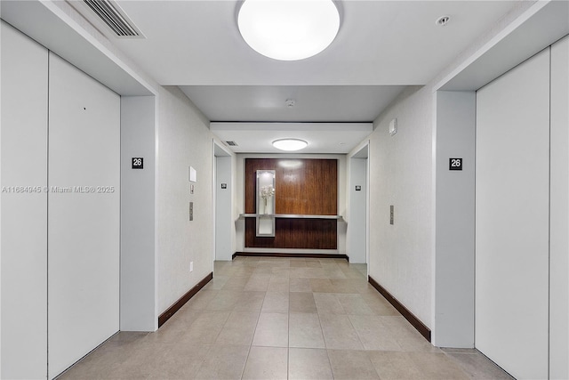 corridor with elevator, visible vents, baseboards, and light tile patterned flooring