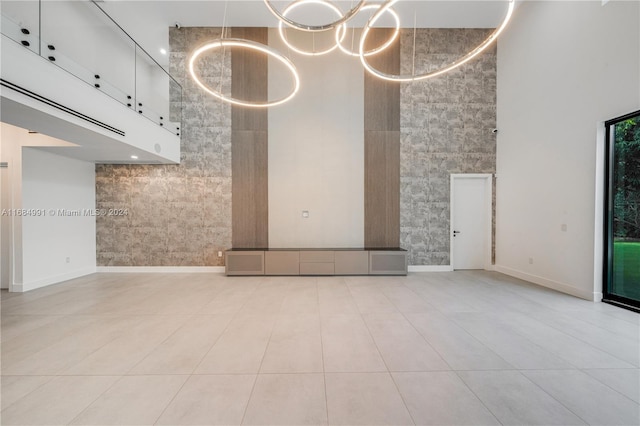 unfurnished living room featuring a towering ceiling, tile walls, light tile patterned floors, and a chandelier