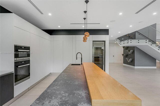 kitchen featuring pendant lighting, stainless steel double oven, white cabinetry, and sink