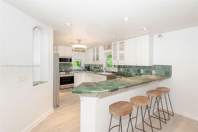 kitchen with white cabinetry, stainless steel appliances, light hardwood / wood-style floors, sink, and kitchen peninsula