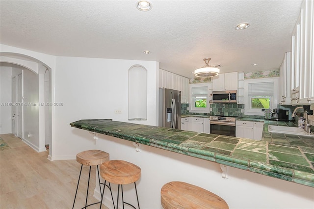 kitchen featuring white cabinetry, kitchen peninsula, stainless steel appliances, a breakfast bar, and sink