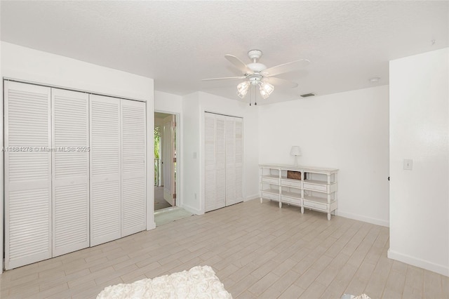 unfurnished bedroom with ceiling fan, a textured ceiling, and two closets