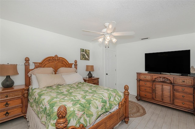 bedroom with a textured ceiling, ceiling fan, and light hardwood / wood-style floors