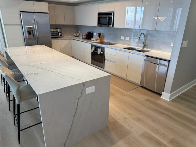 kitchen with sink, light wood-type flooring, backsplash, stainless steel appliances, and pendant lighting