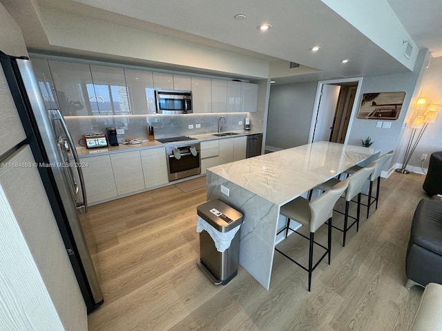 kitchen with stainless steel appliances, a large island, sink, white cabinetry, and light hardwood / wood-style floors