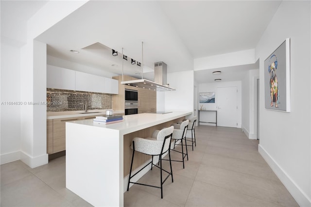 kitchen featuring sink, a kitchen breakfast bar, decorative backsplash, white cabinets, and exhaust hood