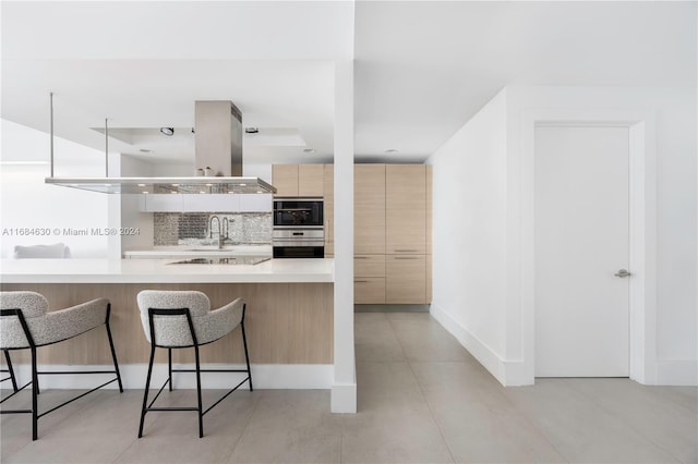 kitchen featuring a kitchen bar, light brown cabinetry, kitchen peninsula, tasteful backsplash, and black electric stovetop