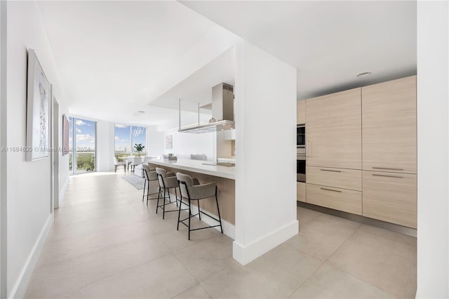 kitchen featuring a breakfast bar, expansive windows, kitchen peninsula, light brown cabinetry, and stainless steel double oven