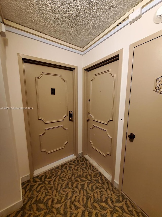 doorway to outside featuring a textured ceiling and dark carpet