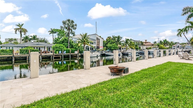 view of dock with a water view, a patio, a lawn, and a fire pit