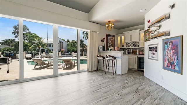 kitchen with white cabinets, tasteful backsplash, beverage cooler, a chandelier, and light hardwood / wood-style floors