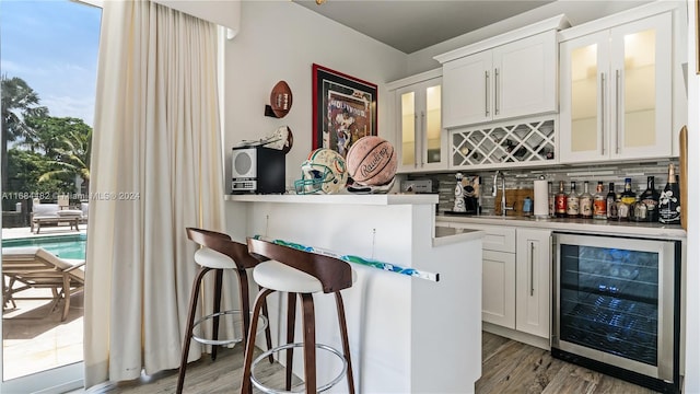 bar with white cabinetry, wine cooler, sink, and backsplash