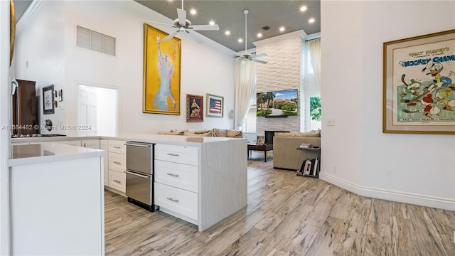 kitchen featuring light hardwood / wood-style floors, white cabinetry, a stone fireplace, and ceiling fan