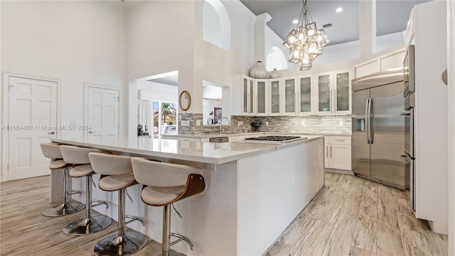 kitchen featuring a towering ceiling, a kitchen island, white cabinetry, stainless steel appliances, and light hardwood / wood-style flooring