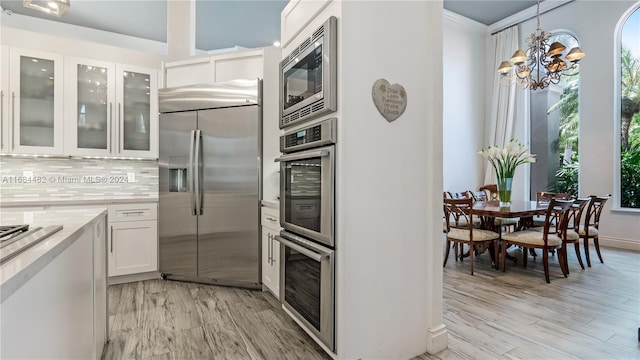 kitchen with decorative backsplash, built in appliances, light hardwood / wood-style flooring, decorative light fixtures, and white cabinetry