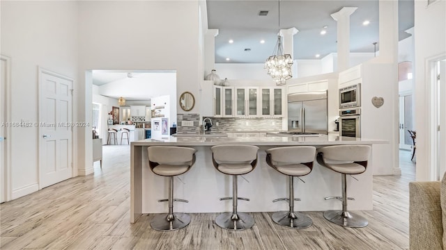 kitchen featuring tasteful backsplash, a towering ceiling, kitchen peninsula, white cabinetry, and built in appliances