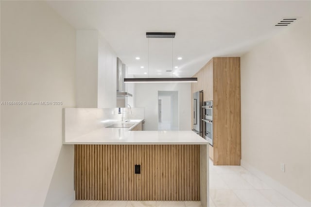 kitchen featuring recessed lighting, a peninsula, light countertops, modern cabinets, and decorative light fixtures