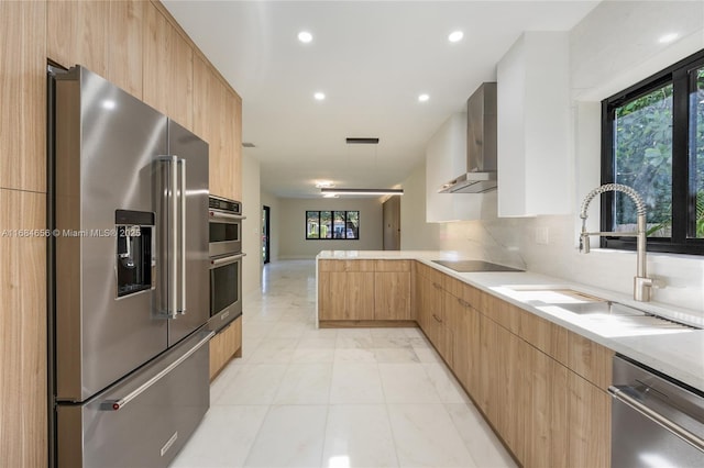 kitchen featuring wall chimney exhaust hood, appliances with stainless steel finishes, modern cabinets, and light brown cabinets