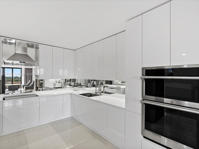 kitchen featuring white cabinetry, wall chimney exhaust hood, and stainless steel double oven