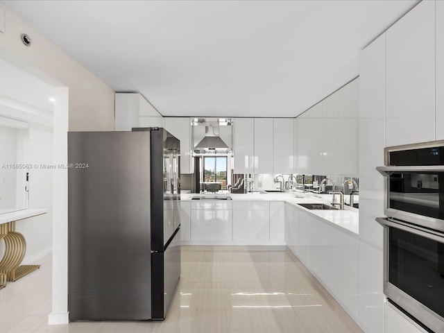 kitchen with wall chimney range hood, sink, light tile patterned flooring, white cabinetry, and stainless steel appliances