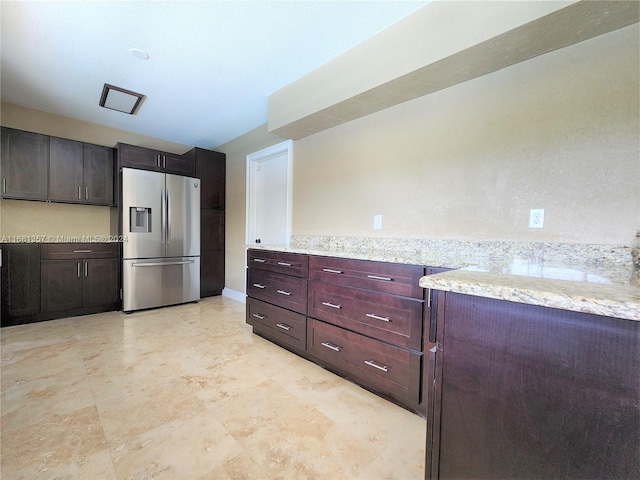 kitchen featuring dark brown cabinetry, stainless steel refrigerator with ice dispenser, and light stone countertops