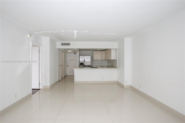 unfurnished living room featuring sink, a textured ceiling, and light tile patterned floors