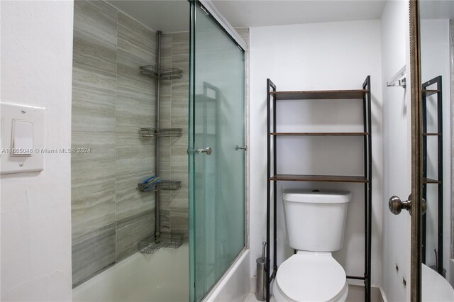 bathroom featuring toilet and shower / bath combination with glass door