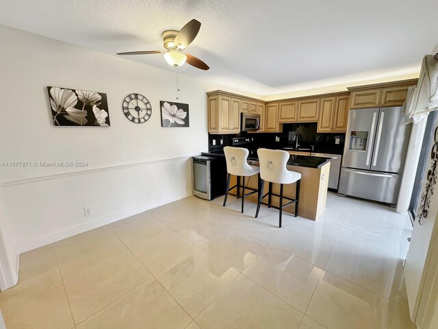 kitchen with tasteful backsplash, appliances with stainless steel finishes, a kitchen bar, a textured ceiling, and light tile patterned floors