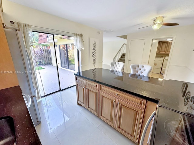 kitchen featuring washer and clothes dryer, ceiling fan, white refrigerator, and dark stone counters