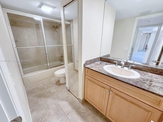 full bathroom with a textured ceiling, toilet, enclosed tub / shower combo, vanity, and tile patterned flooring