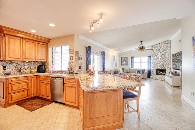 kitchen featuring ornamental molding, a stone fireplace, dishwasher, and a breakfast bar area