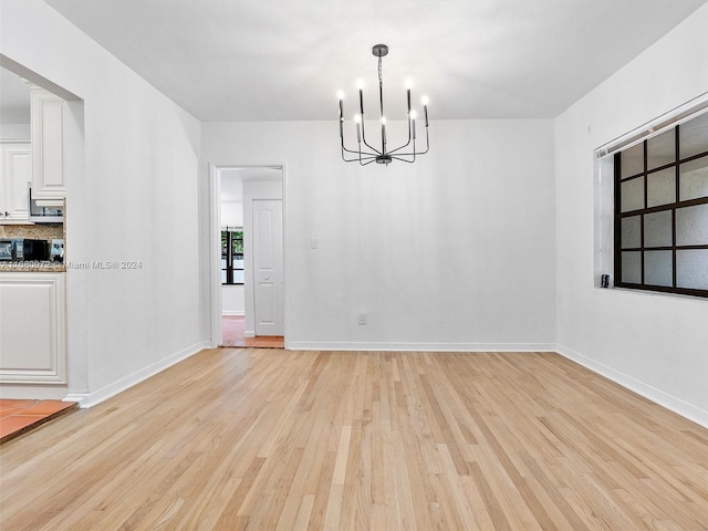 unfurnished dining area with a chandelier and light wood-type flooring