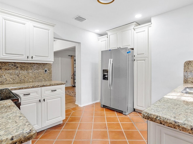 kitchen featuring white cabinets, stainless steel refrigerator with ice dispenser, light tile patterned floors, and tasteful backsplash